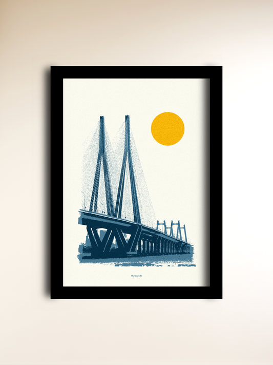 A framed minimalist art print of the Mumbai Sea Link, featuring a blue illustration of the bridge and water under a yellow sun on a cream background, housed in a black frame and mounted on a beige wall.