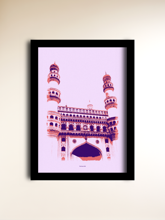 A framed art print of the Charminar in Hyderabad, rendered in a stylized pink and purple pop-art design, set in a black frame against a light beige wall.